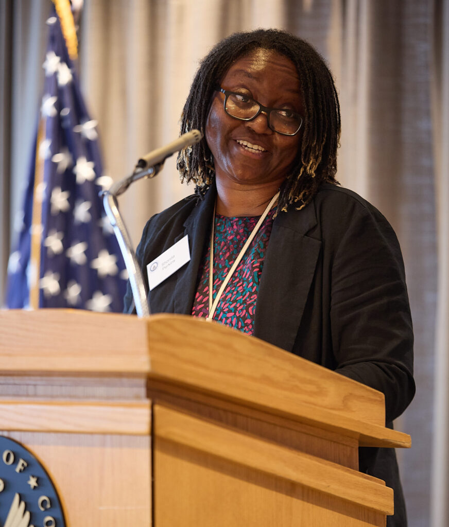 A woman stands behind a podium, speaking into a microphone