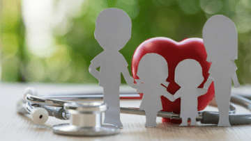 paper cut outs of 2 parents and 2 children standing hand-and-hand with a heart and stethoscope in the back and fore ground