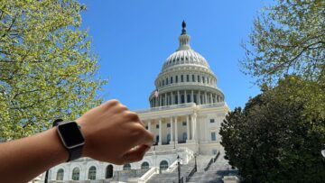 An arm with a smartwatch on its wrist is raised in front of the U.S. Capitol building