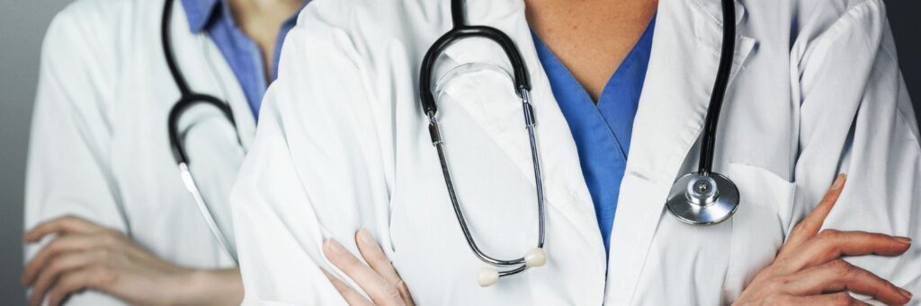 Two doctors wearing lab coats and stethoscopes standing with their arms folded across their chests