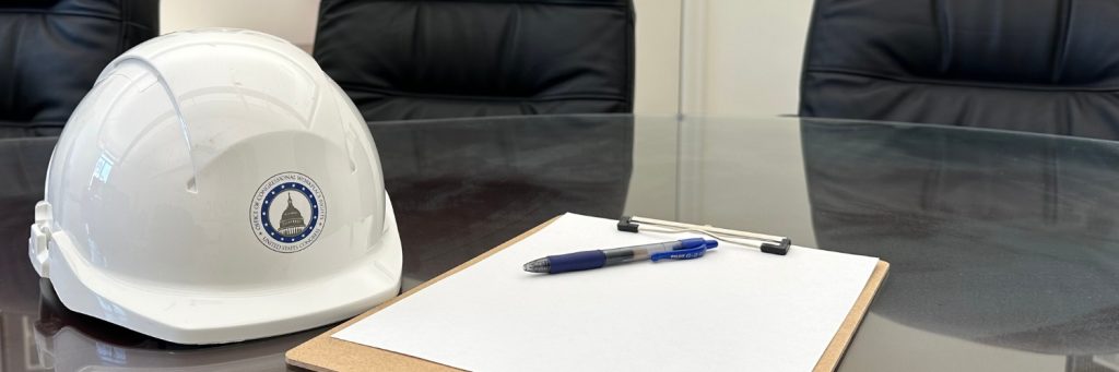 A hard hat and clipboard rest on a conference table