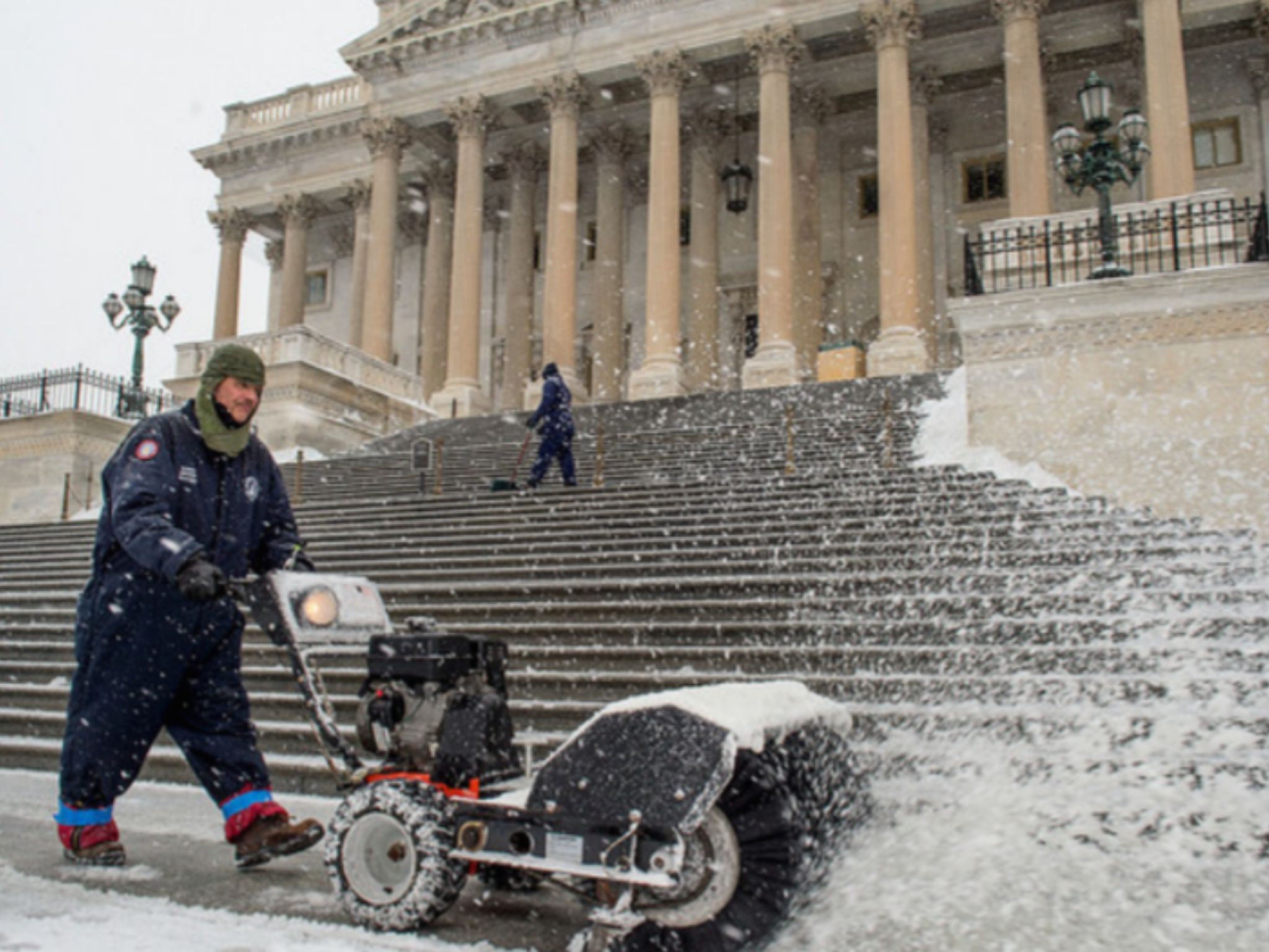 a person blowing snow with a machine in front of a Capitol Hill building