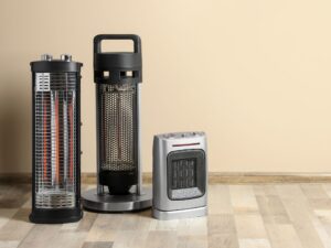 Three space heaters of varying sizes sit on top of a wood-paneled floor