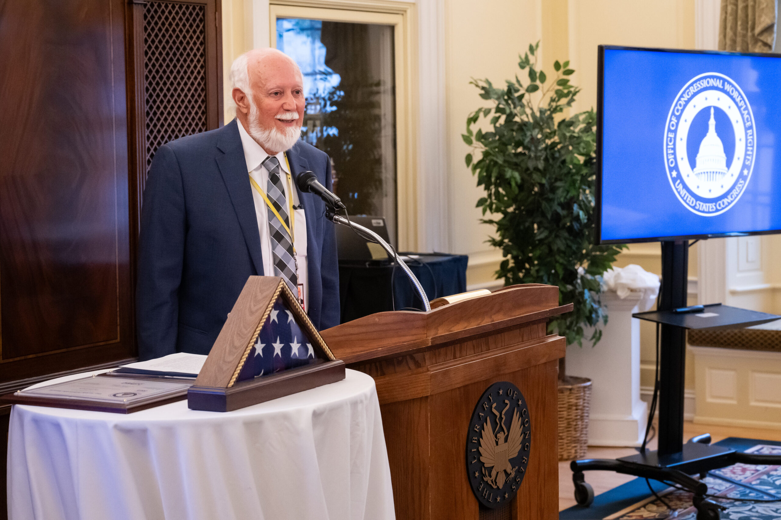 Man stands at a podium next to a table with a framed U.S. flag