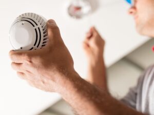 A man installs a smoke detector on the ceiling in an office
